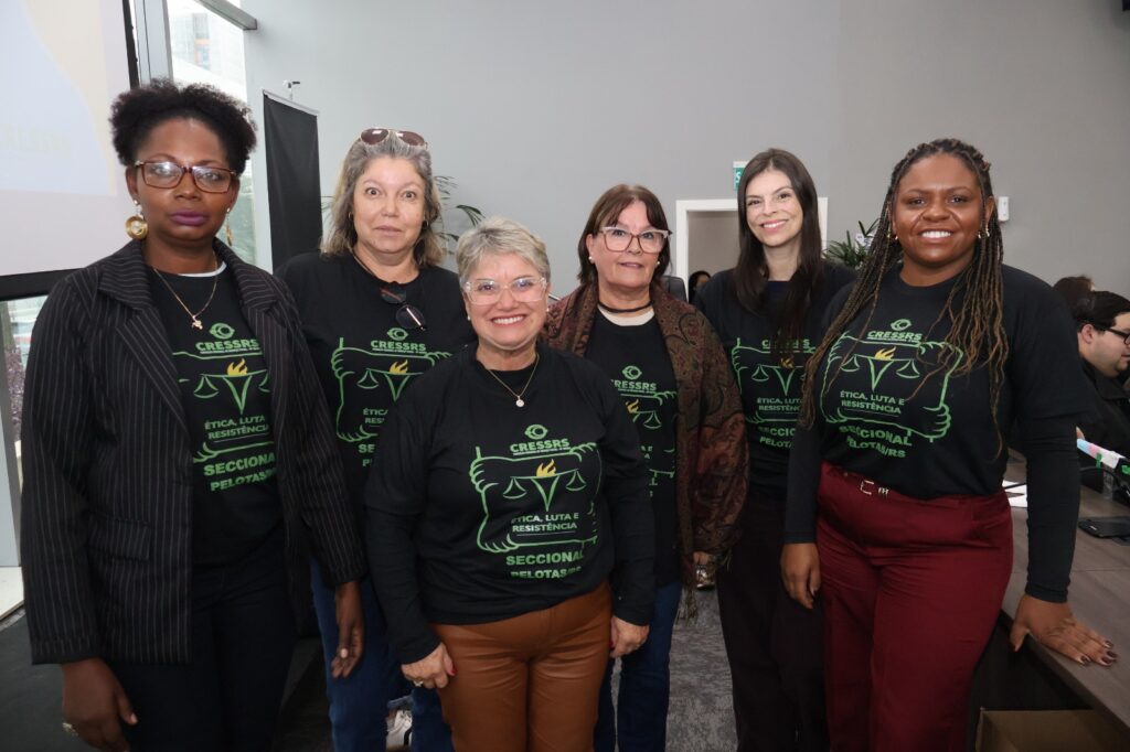 Fotografia no auditório da OAB, com a presença de duas mulheres, negras, e quatro mulheres, brancas. Elas estão de pé lado a lado e vestem uma camisa preta com a marca da chapa que concorreu a gestão do Cress "Ética, luta e resistência".