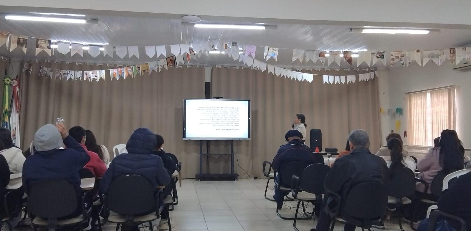 fotografia da conselheira do CRESSRS apresentando um telão na conferência de Camargo, com plateia observando.