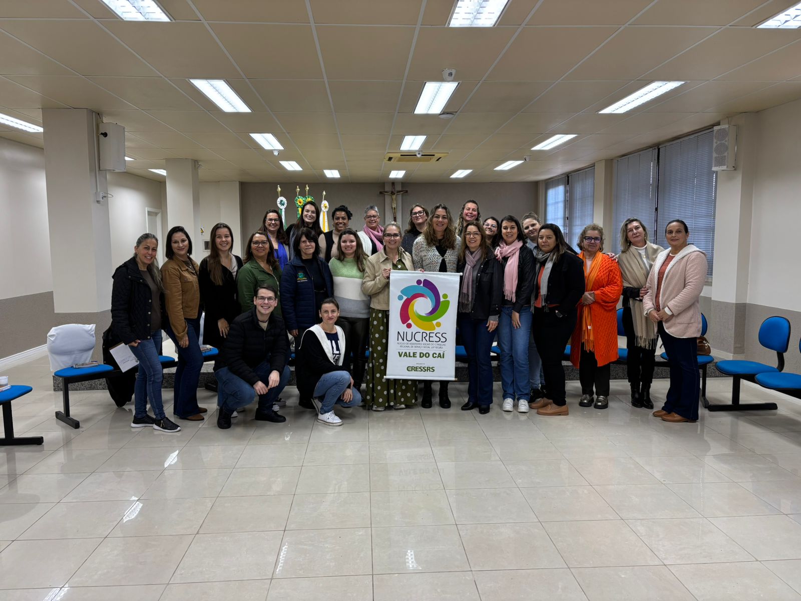 fotografia com cerca de 24 pessoas, na maioria mulheres, brancas. Elas seguram um banner do NUCRESS. Em texto, NUCRESS Vale do Caí reúne-se em Feliz (RS).