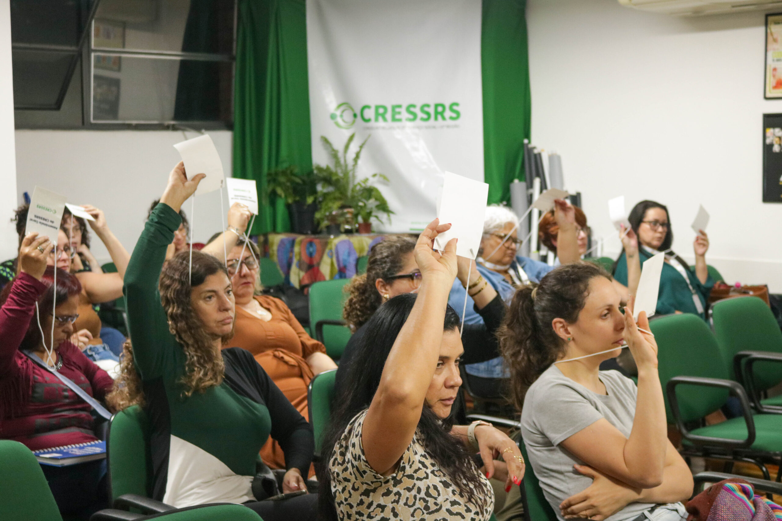 Oito mulheres levantam um crachá durante assembleia na sede do CRESSRS.