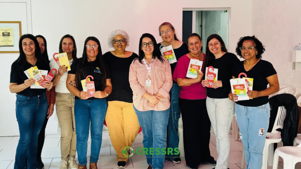 Fotografia com dez mulheres, de pé, segurando o livro "Bandeira de Lutas" do conjunto CFESS-CRESS. Elas são brancas e negras, todas de cabelos pretos, uma de cabelos brancos. 