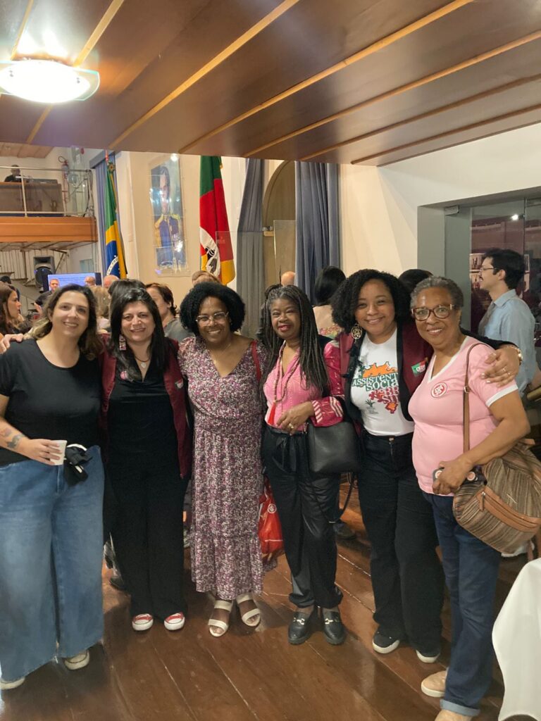 Seis mulheres, na qual quatro são negras, estão de pé reunidas no salão da Assembleia Legislativa. 