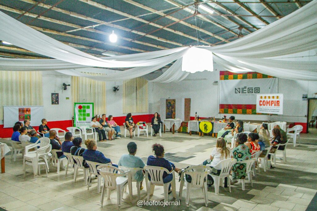 25 pessoas sentadas em roda, em auditório. Nas paredes, estão pendurados banners do COMPIR, IF SUL e NEGO.