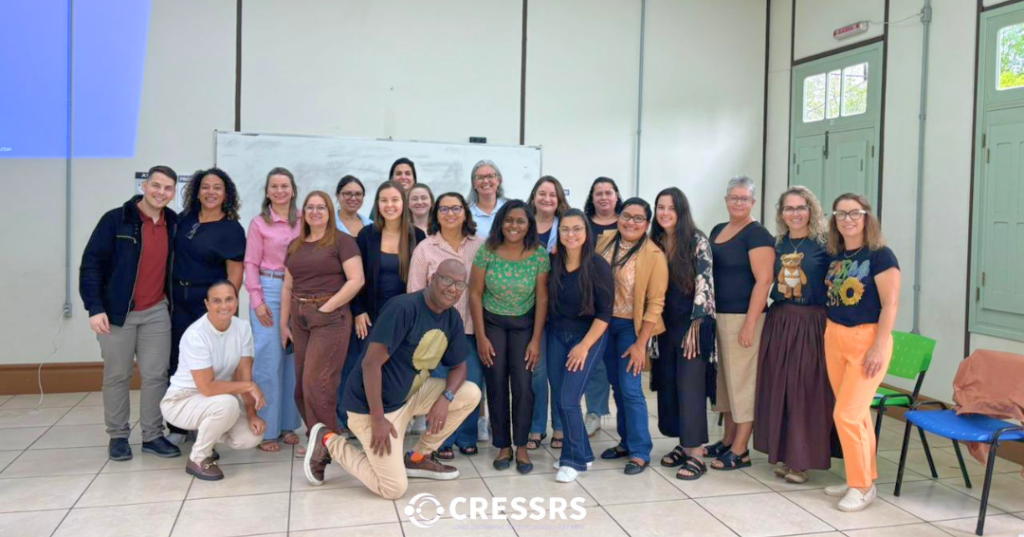 Fotografia com 21 profissionais, 2 homens e 19 mulheres. Um homem negro e uma mulher negra estão ao centro da foto.