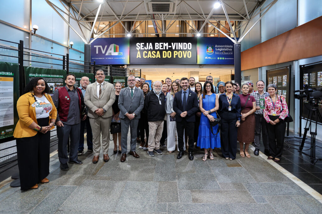 26 pessoas reunidas no saguão da Assembleia Legislativa do RS. No canto esquerdo, presente a vice-presidenta do CRESSRS, mulher, negra, cabelos crespos e curtos.