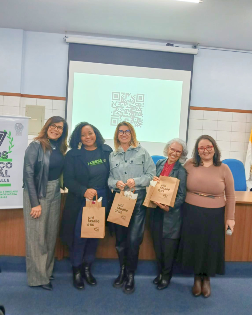 Fotografia com 5 mulheres, uma negra e quatro brancas, segurando presentes e posando para a foto.